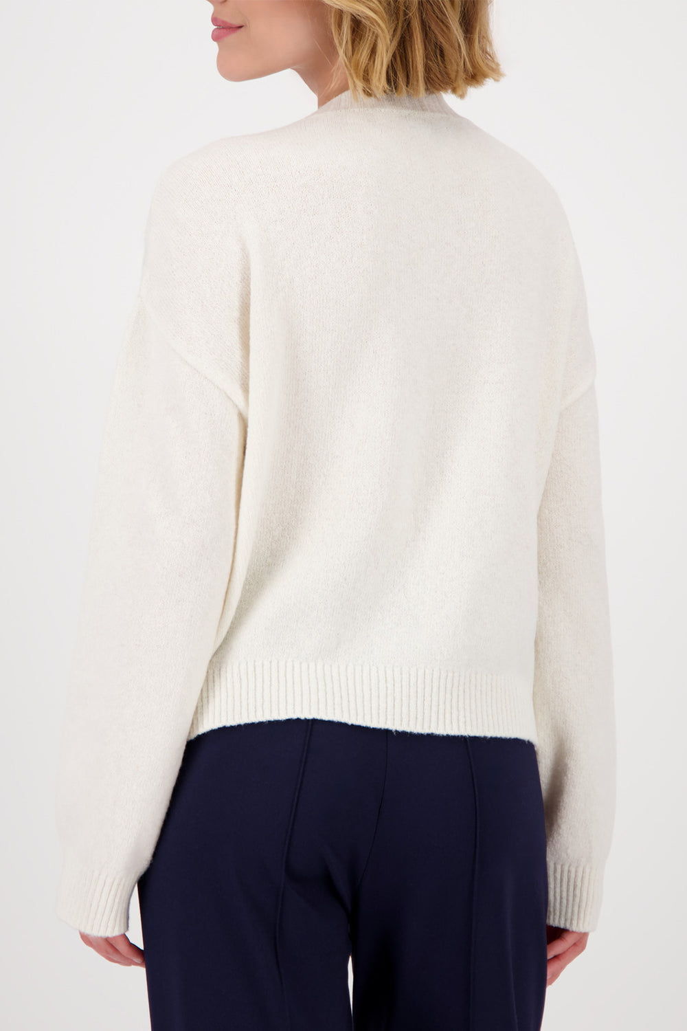 Person wearing a white sweater and navy pants on a white background