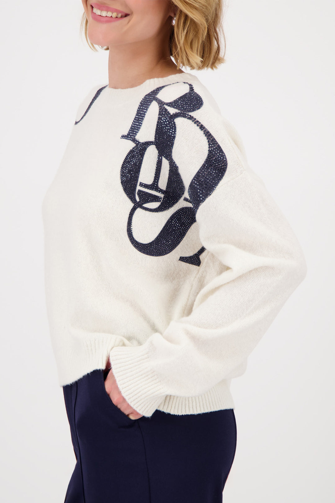 Person wearing a white sweater with a navy logo on a light gray background