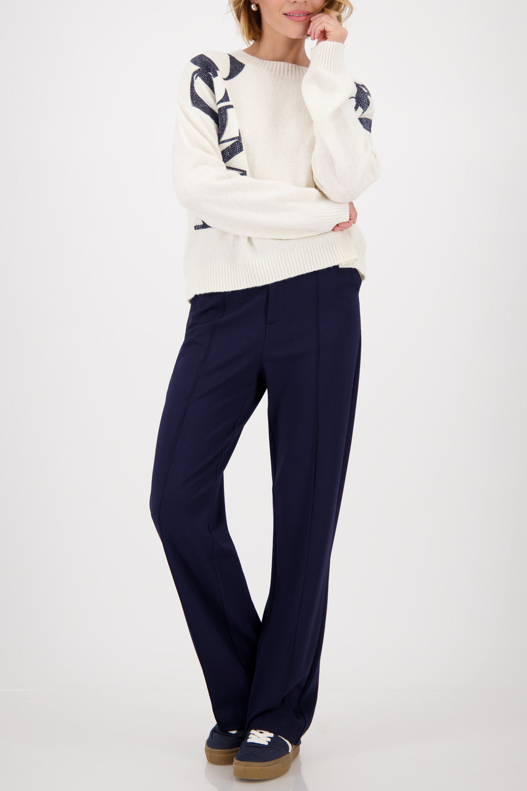 Person wearing a white sweater with navy patterns and navy pants on a white background