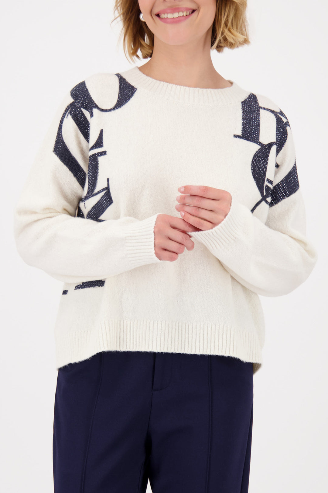 Person wearing a white sweater with blue patterns and navy pants on a white background