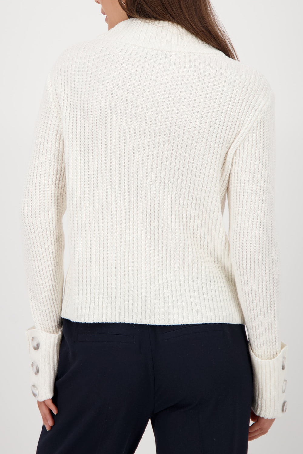 Person wearing a white ribbed sweater with button details on a plain background