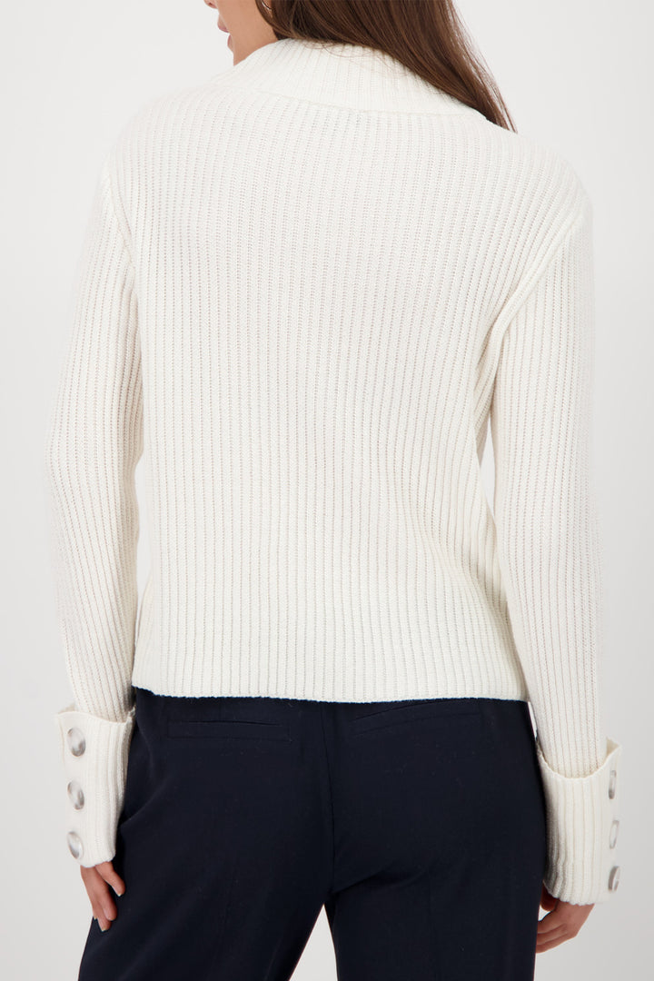 Person wearing a white ribbed sweater with button details on a plain background