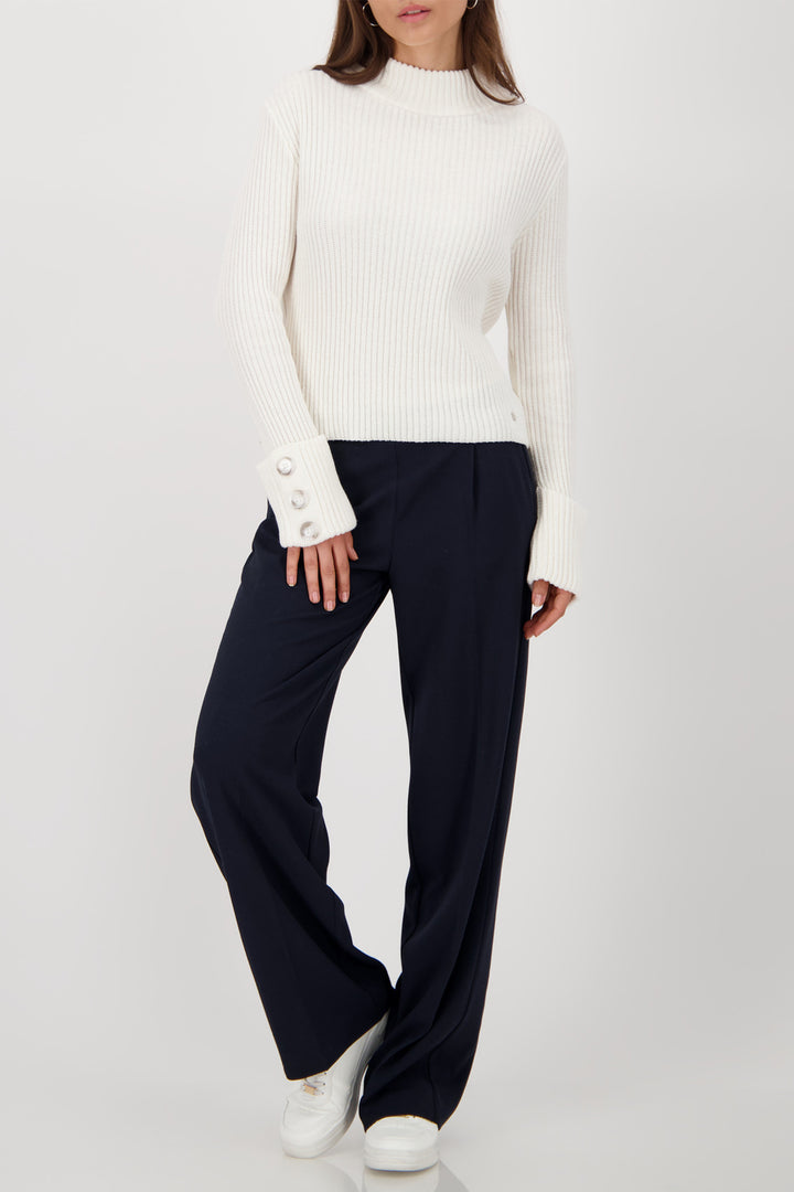 Person wearing a white sweater and navy pants on a white background