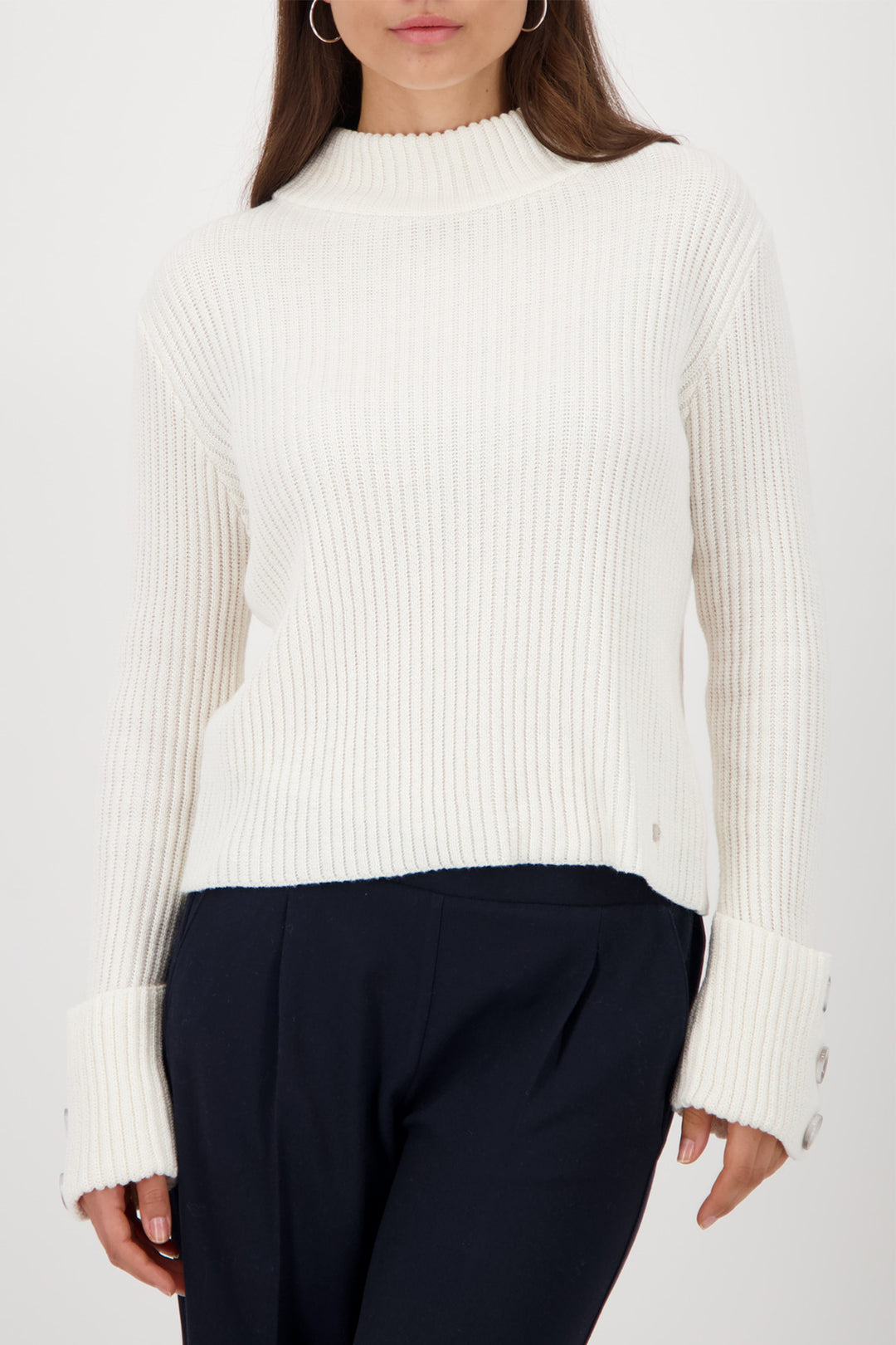 Person wearing a white ribbed sweater and dark pants on a white background