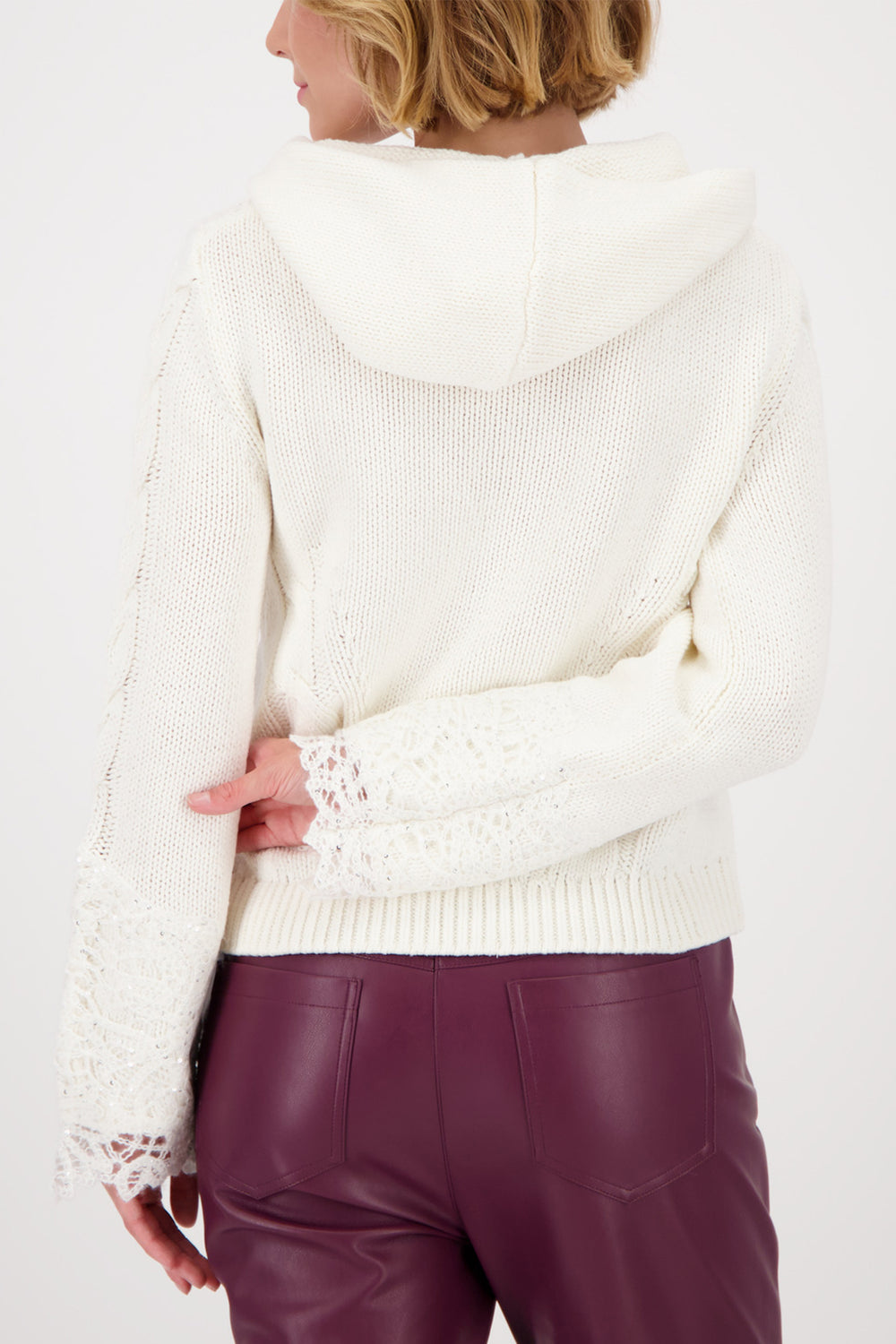 Person wearing a white sweater and maroon pants on a plain background