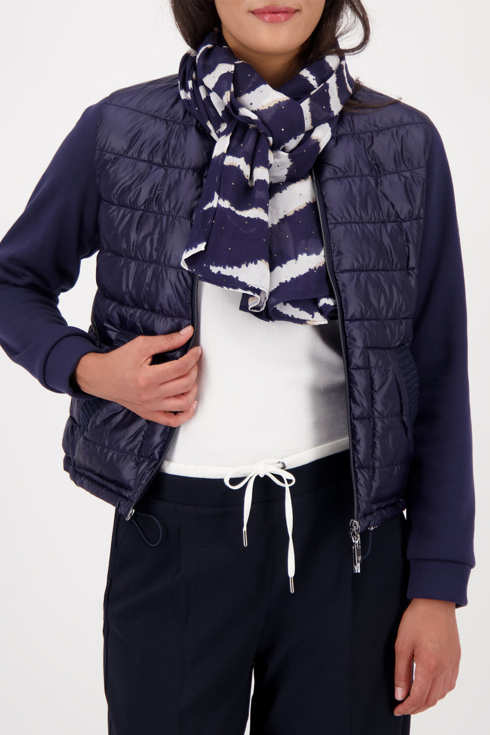 Person wearing a navy puffer vest, white shirt, black pants, and a navy and white patterned scarf on a white background