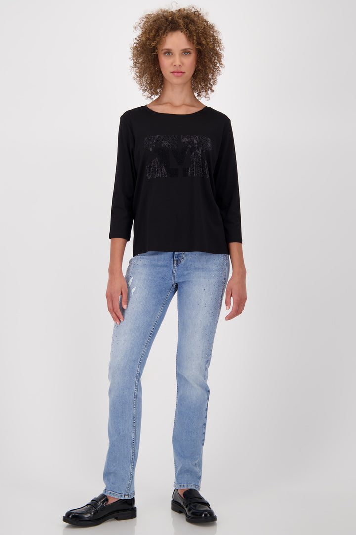 Woman wearing a black long-sleeve top and light blue jeans on a white background