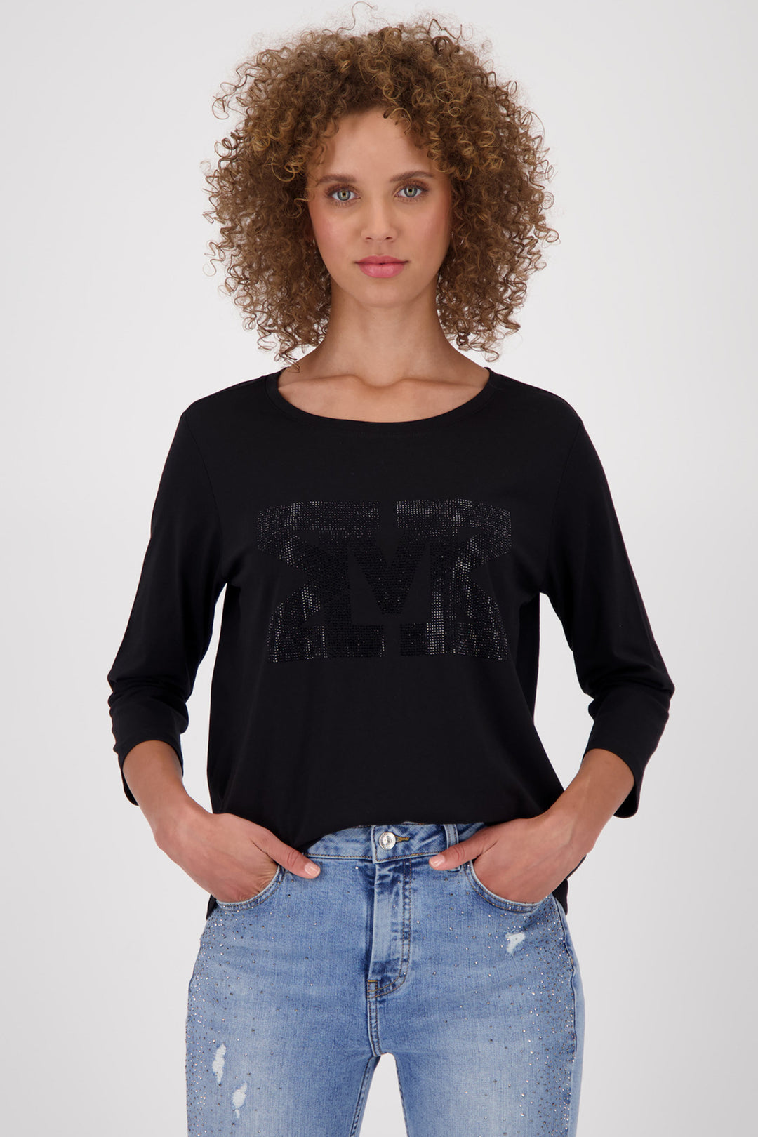 Woman wearing a black top and blue jeans against a white background