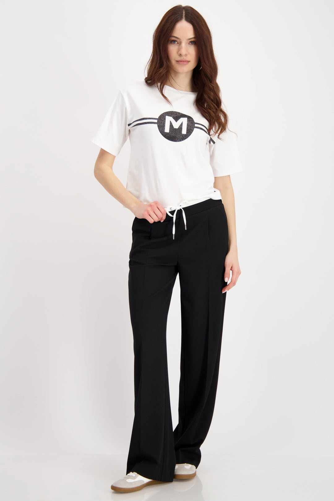 Woman wearing a white t-shirt with a logo and black pants on a white background