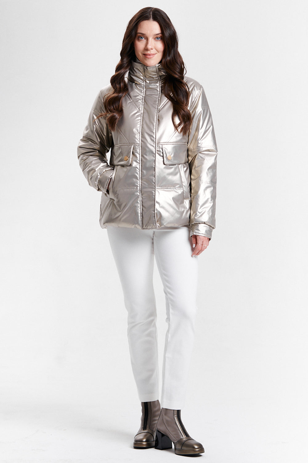 Woman wearing a silver metallic jacket and white pants on a white background