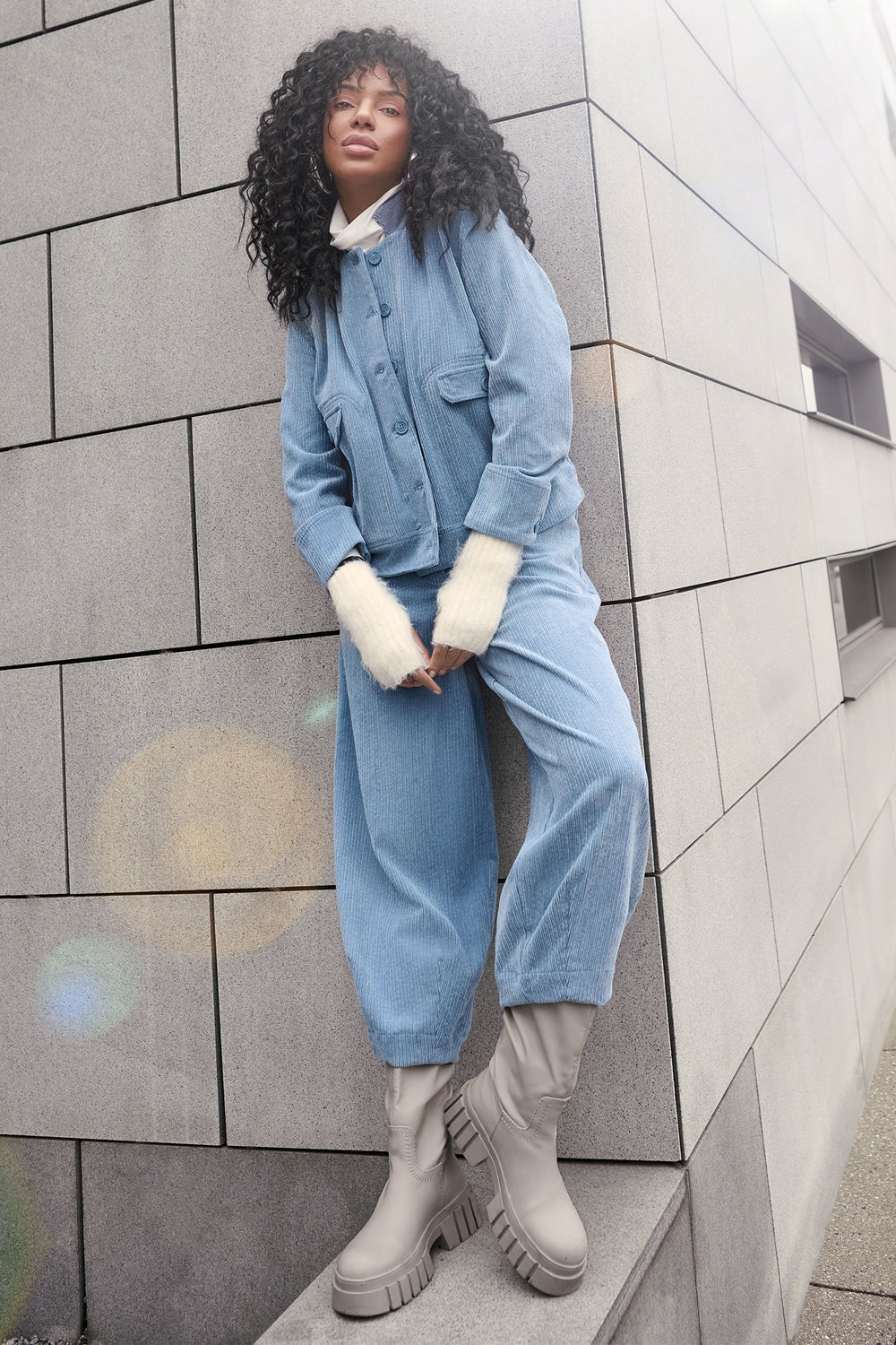 Person wearing a blue denim outfit standing against a tiled wall.