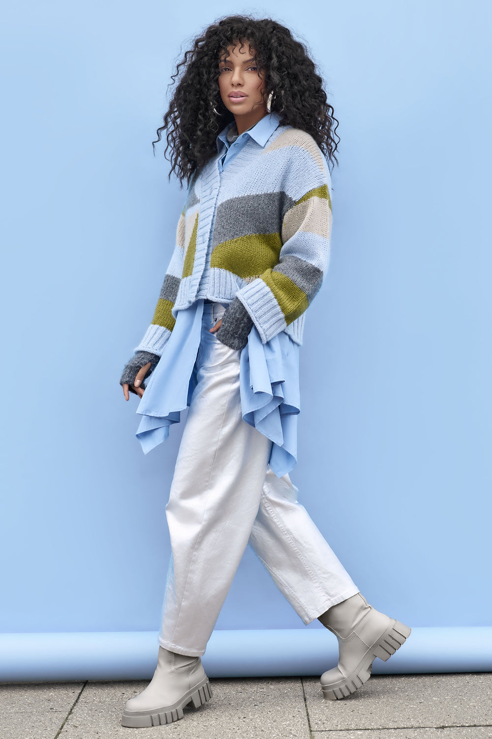 Person wearing a colourful sweater and silver jeans against a blue background