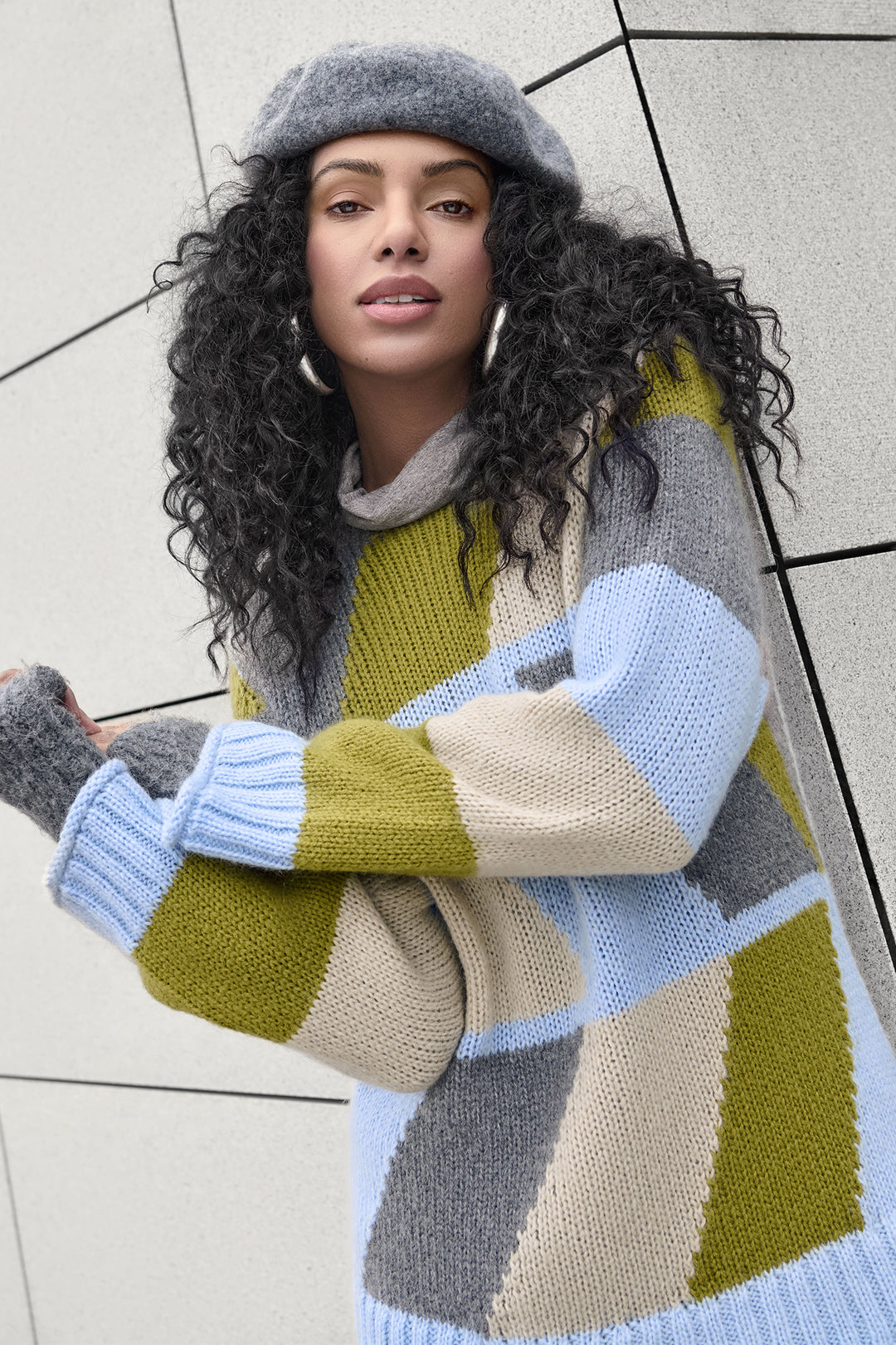 Woman wearing a colorful striped sweater and beret against a tiled wall.