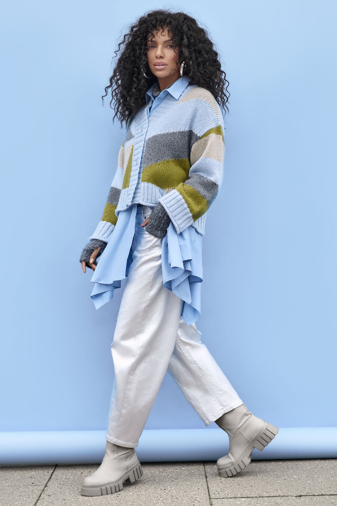 Woman wearing a colorful sweater and light pants against a blue wall