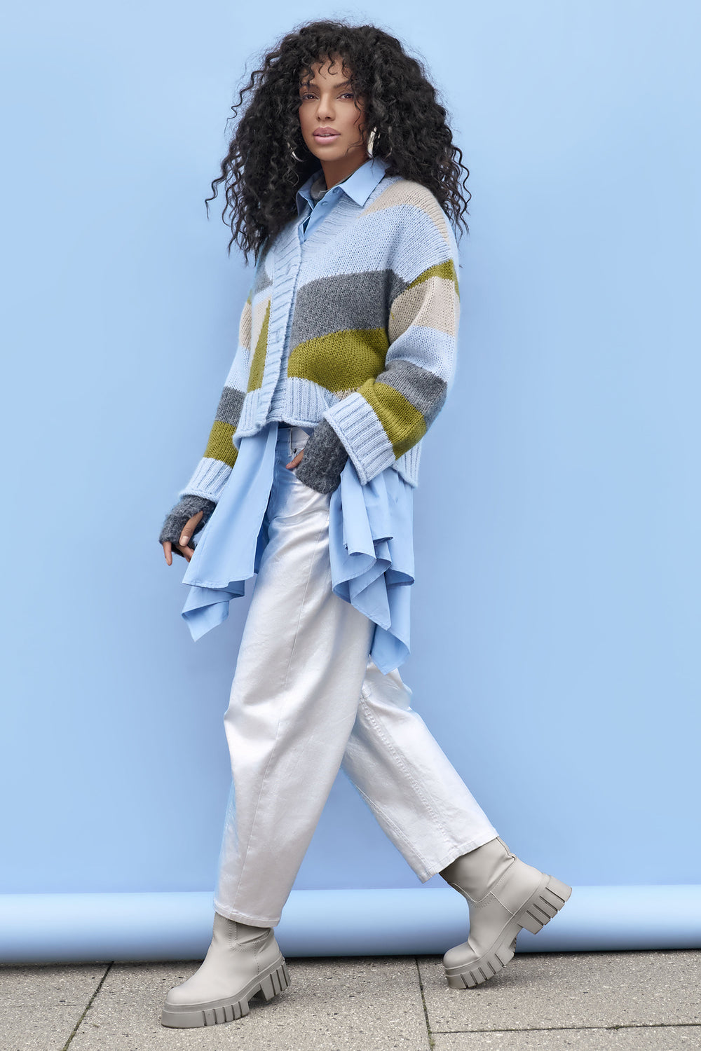 Woman wearing a colorful striped sweater over a blue shirt against a light blue wall.