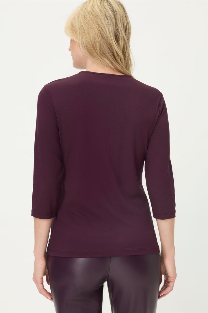 Person wearing a burgundy long-sleeve top and dark pants on a white background