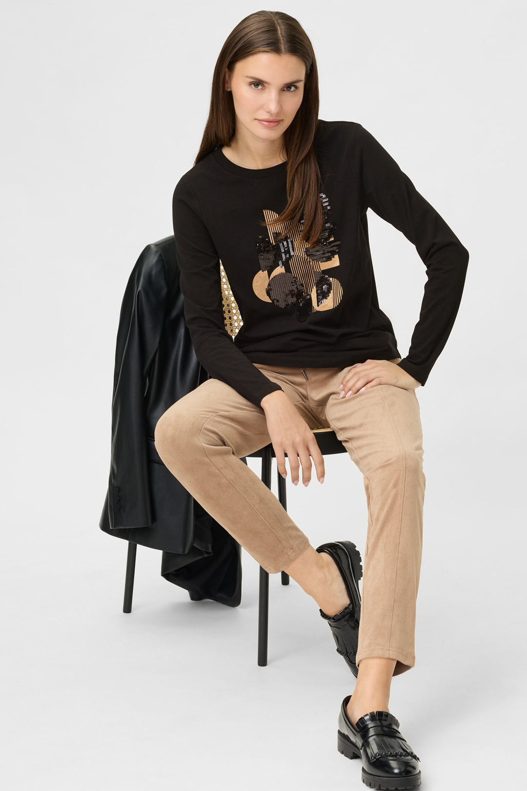 Woman sitting on a chair wearing a black sweater with a fox design and beige pants.
