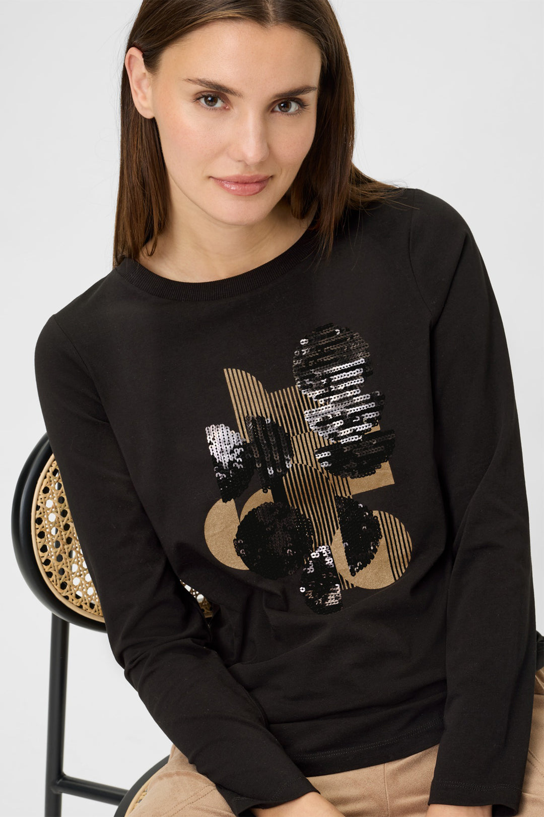Woman wearing a black sweatshirt with a gold and black design, sitting on a chair.
