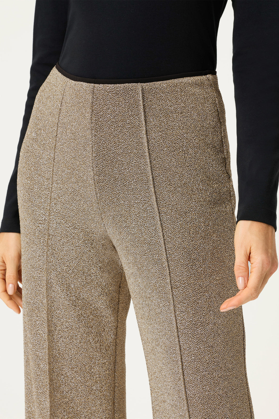 Gold textured pants worn with a black top on a white background