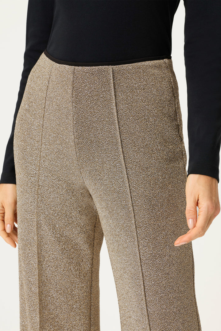 Gold textured pants worn with a black top on a white background