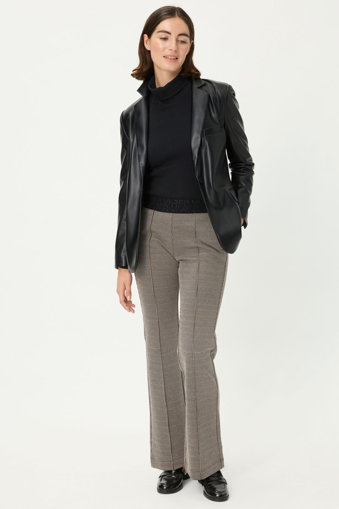 Woman wearing a black blazer, black turtleneck, and gray checkered pants on a white background