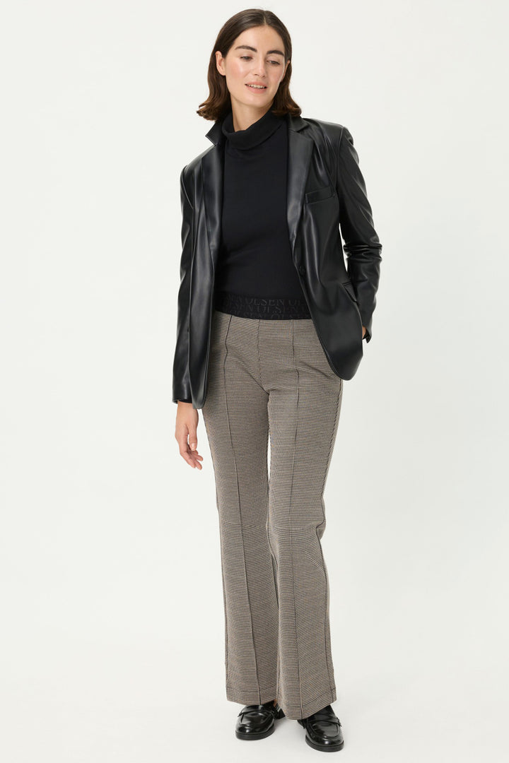 Woman wearing a black blazer, black turtleneck, and gray checkered pants on a white background