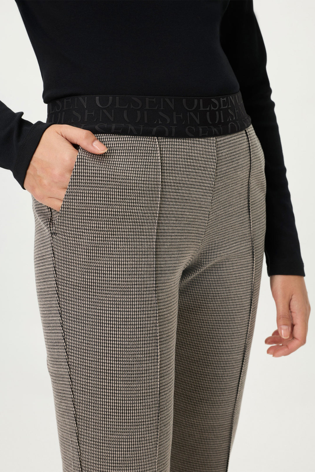 Person wearing a black sweater and gray checkered pants on a white background