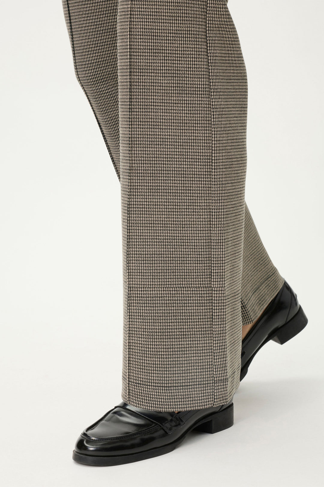 Person wearing brown checkered pants and black shoes on a white background