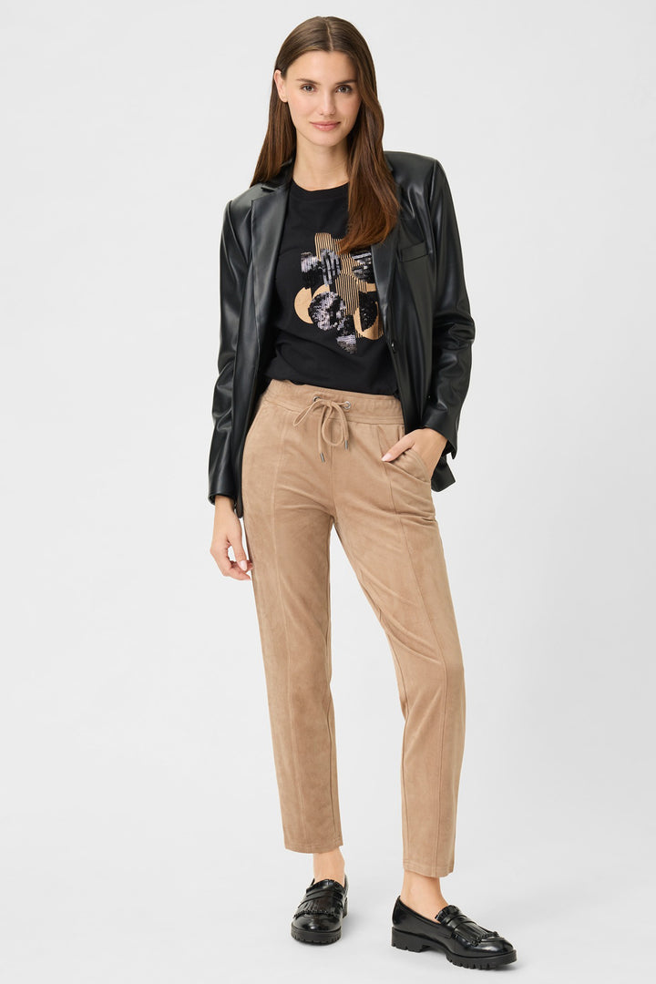 Woman wearing a black leather jacket, black graphic t-shirt, and beige pants on a white background