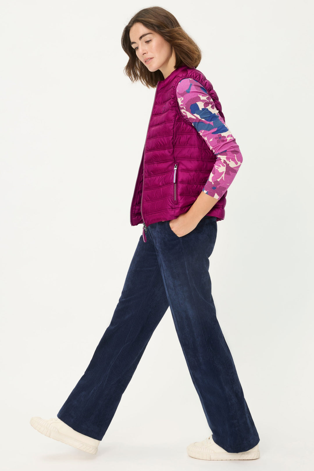 Woman wearing a purple puffer vest over a colorful shirt with navy pants on a white background