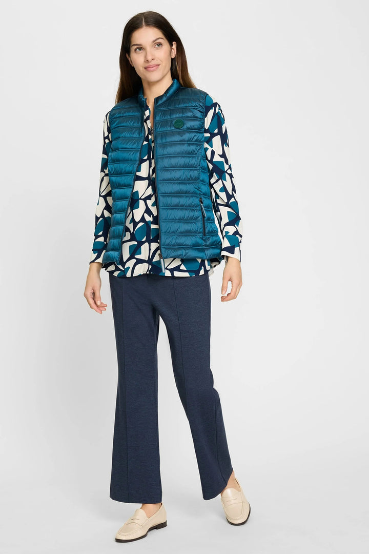 Woman wearing a blue puffer vest over a patterned shirt with navy pants on a white background
