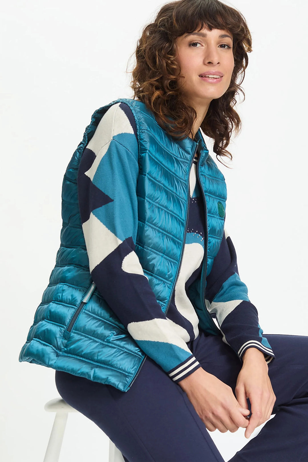 Woman wearing a blue and white quilted jacket sitting on a chair against a white background