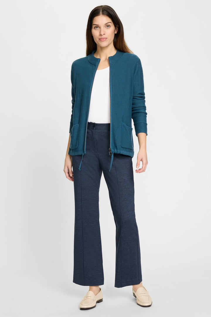 Woman wearing a teal cardigan, white shirt, and navy pants on a white background