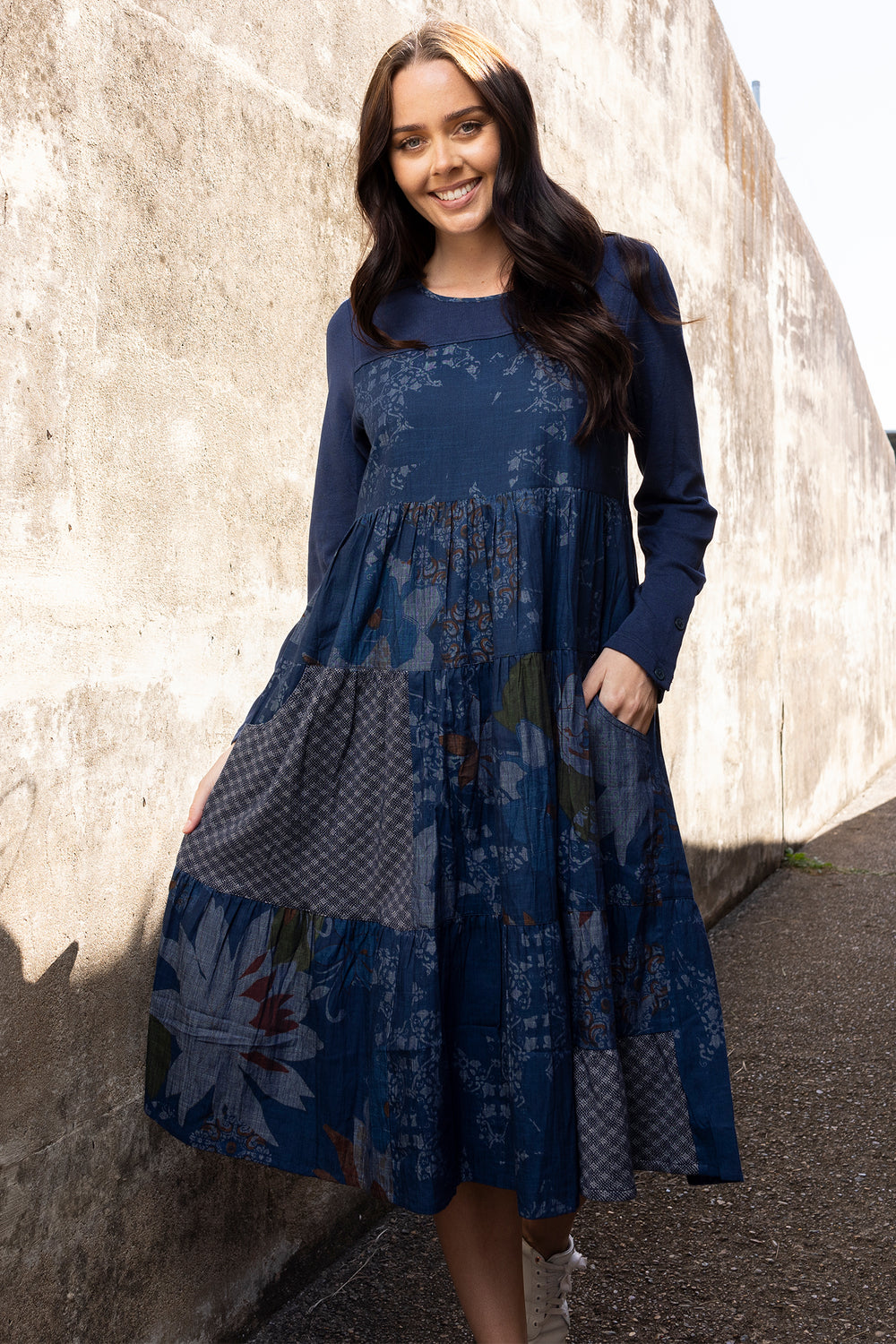 Woman wearing a blue floral dress standing against a textured wall.