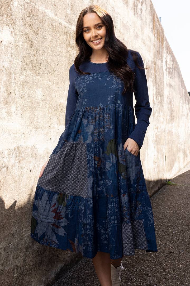 Woman wearing a blue floral dress standing against a textured wall.