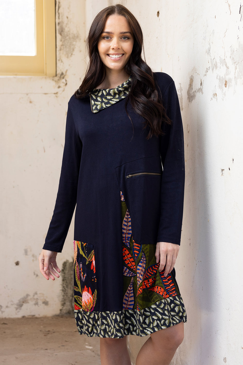 Woman wearing a navy dress with colorful patterns against a textured wall.