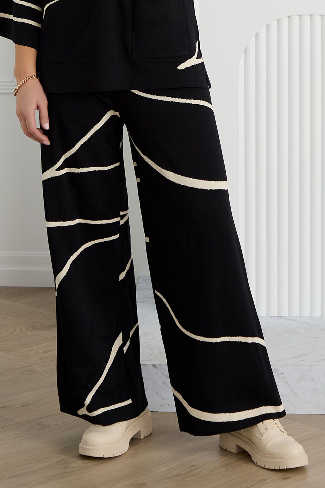Person wearing black pants with white stripes and beige shoes indoors.