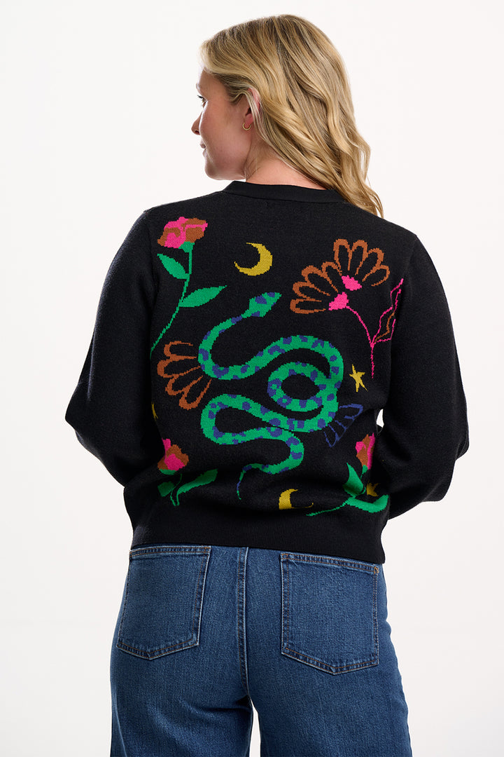 Person wearing a black sweater with colorful snake design on the back, standing against a white background.