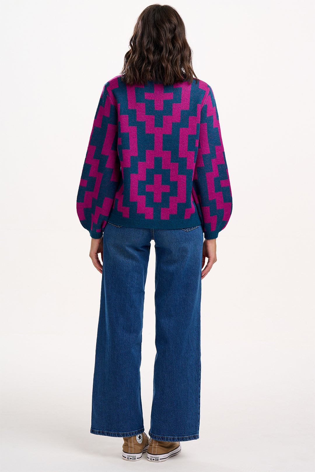 Person wearing a patterned sweater and blue jeans on a white background