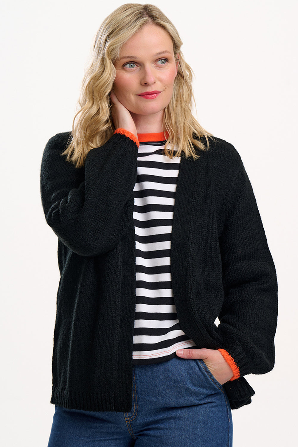 Woman wearing a black cardigan over a striped shirt with blue jeans on a white background