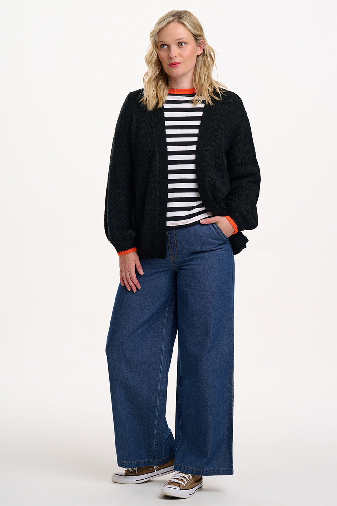 Woman wearing a black cardigan, striped shirt, and blue jeans on a white background