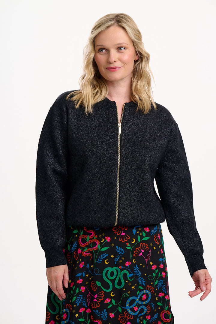 Woman wearing a black zip-up sweater over a colorful patterned skirt on a white background