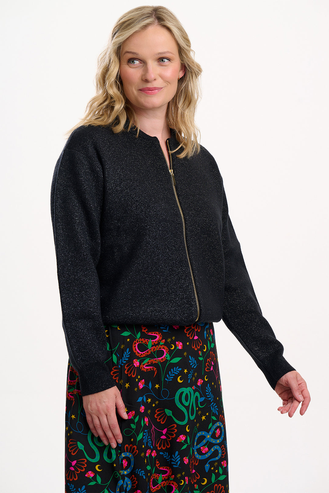 Woman wearing a black jacket with a colorful patterned skirt on a white background
