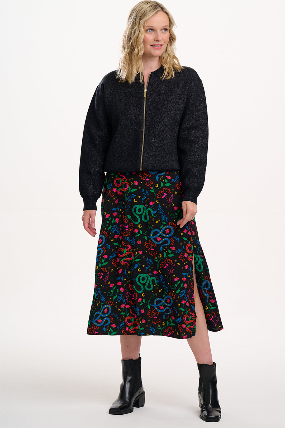 Woman wearing a black jacket and colorful patterned skirt on a white background