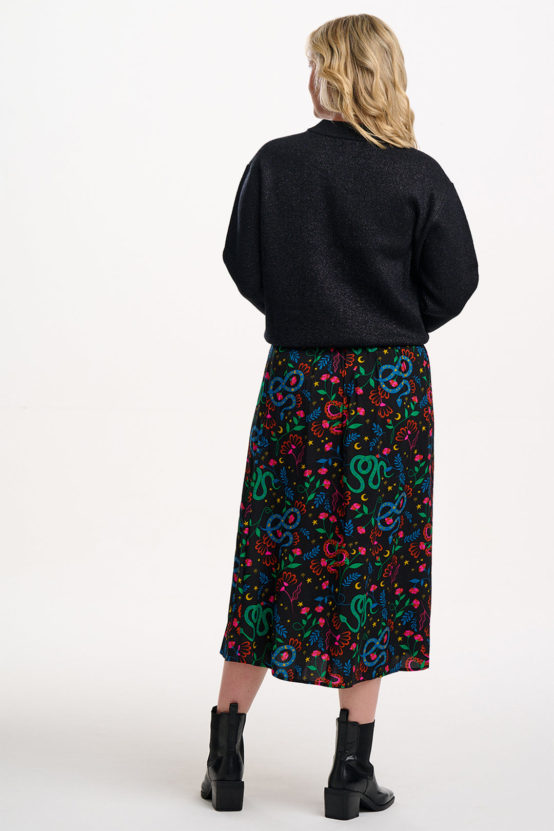 Person wearing a black sweater and colorful patterned skirt on a white background