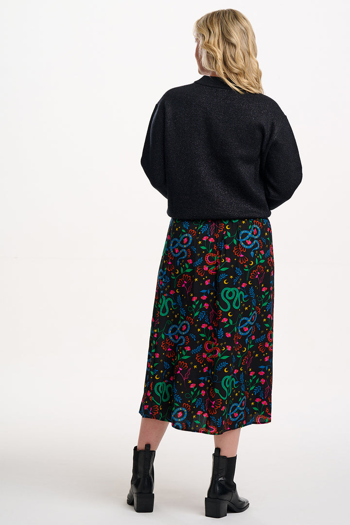 Person wearing a black sweater and colorful patterned skirt on a white background