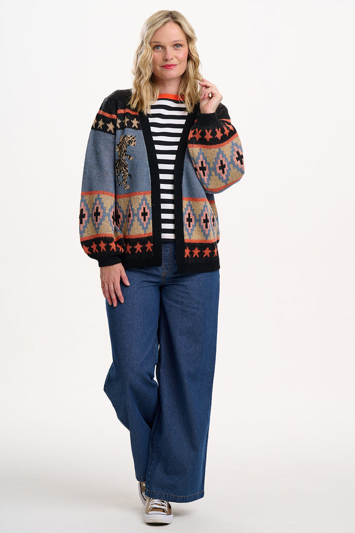 Woman wearing a patterned cardigan, striped shirt, and blue pants on a white background