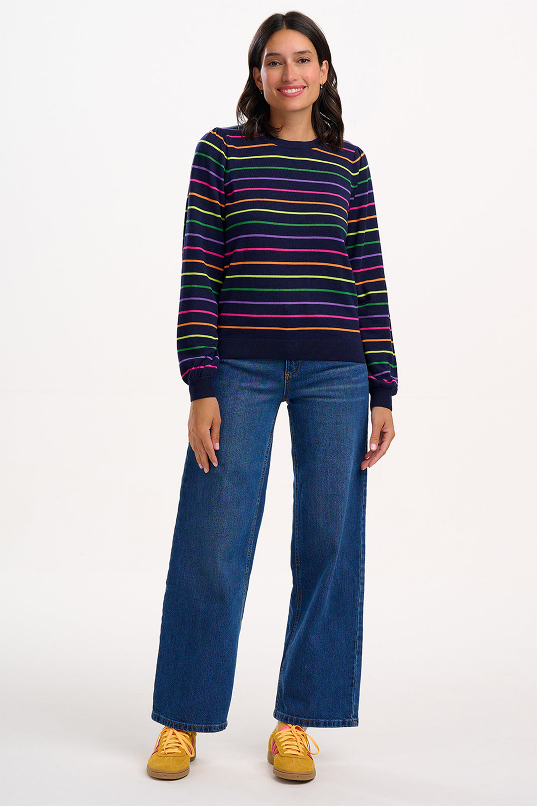 Person wearing a colorful striped sweater and blue jeans on a white background
