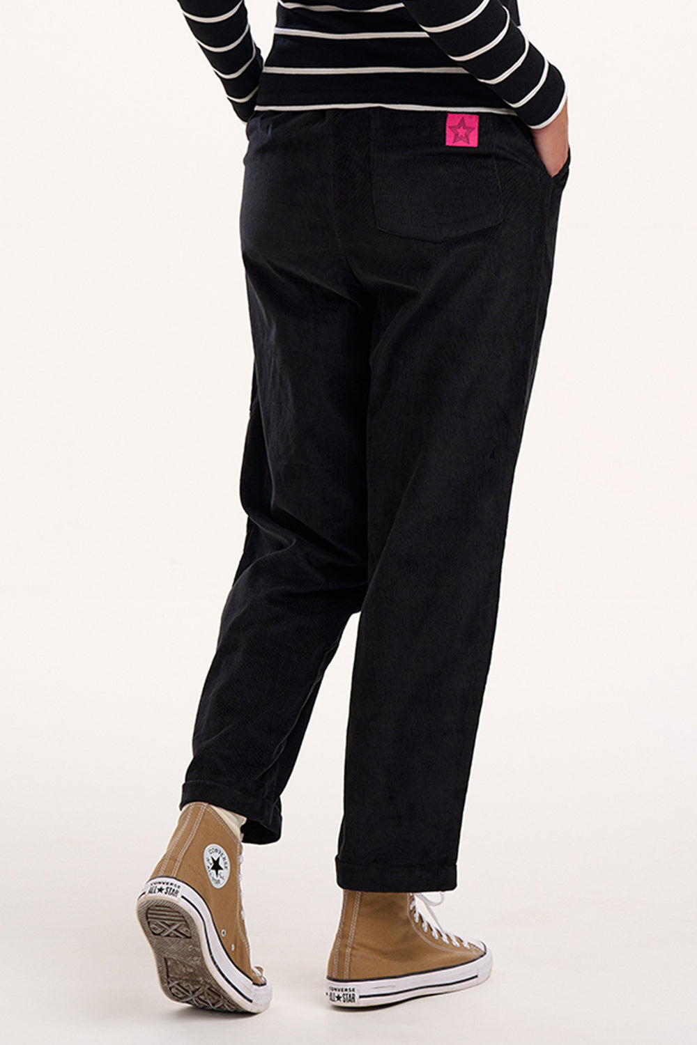 Person wearing black pants and a striped shirt with a pink tag on a white background