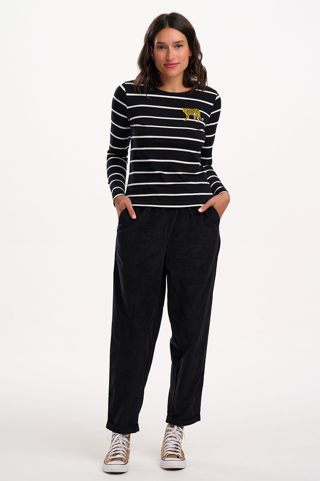 Woman wearing a black and white striped shirt with a yellow logo and black pants on a white background